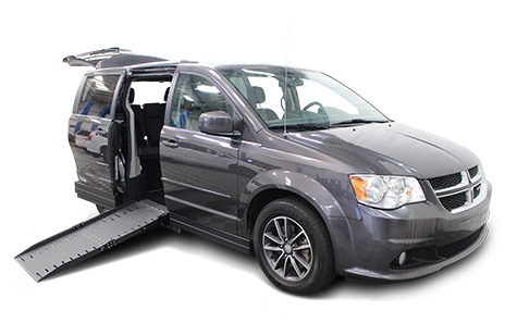 A gray Dodge Grand Caravan with AMS wheelchair van conversion with ramp deployed from open passenger sliding doorway.