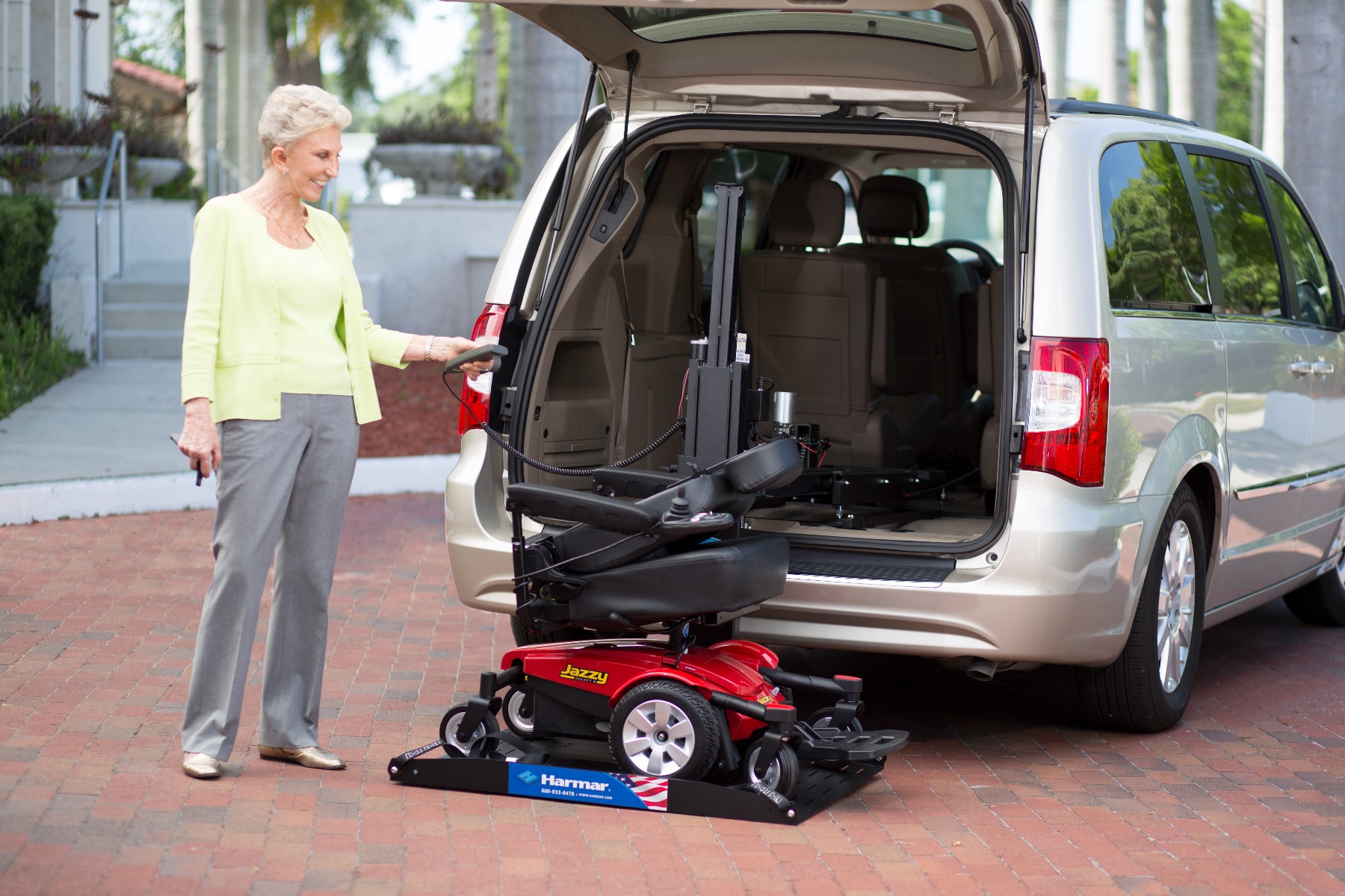Woman using a Harmar lift to load a power wheelchair into a gold minivan.
